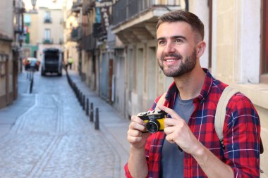 Eski şehir caddesinde sırt çantalı ve klasik kameralı yakışıklı bir gencin yakın plan portresi.
