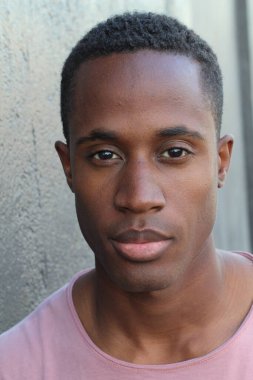 Gri duvarın önünde pembe tişörtlü yakışıklı genç adamın yakın plan portresi.