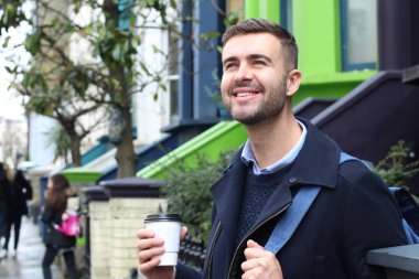 Sokakta elinde kağıt bardak kahveyle ceketli yakışıklı bir gencin yakın plan portresi.