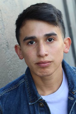 Gri beton duvarın önünde sıradan kıyafetler giymiş yakışıklı genç adamın yakın plan portresi.