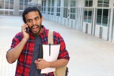 close-up portrait of handsome young mixed race student in red plaid shirt talking by phone on street