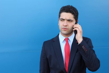 Mavi duvarın önünde telefonla konuşan yakışıklı genç iş adamının yakın plan portresi.