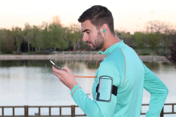 close-up portrait of handsome young jogger with smartphone and earphones in front of lake in park