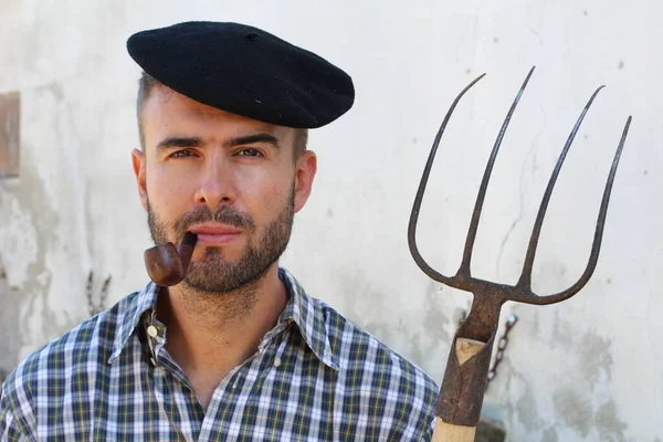 close-up portrait of handsome young farmer with Pitchfork in front of house wall