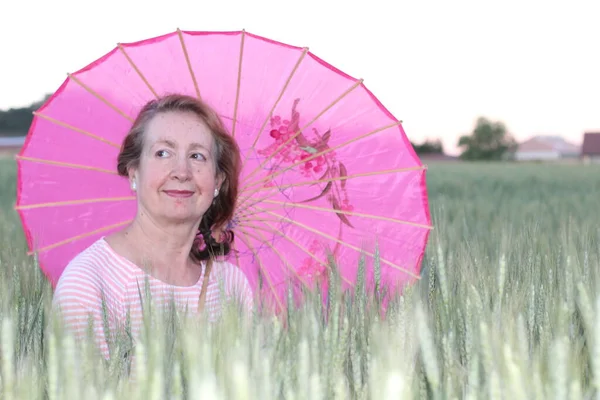 阳光普照的日子 一个成熟的女人拿着粉红的雨伞 — 图库照片