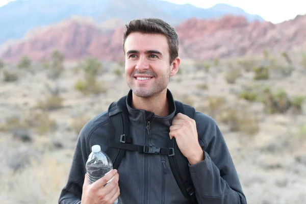 Smiling man with backpack and bottle of water on nature background