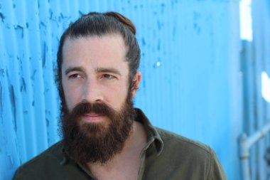 Tarz sahibi sakallı hippi erkek saç stili, sokakta yaşam tarzı, tarlanın derinliği. Mavi arkaplan