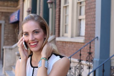 Güzel, güler yüzlü bir sarışın şehir dışında telefonla konuşuyor. 