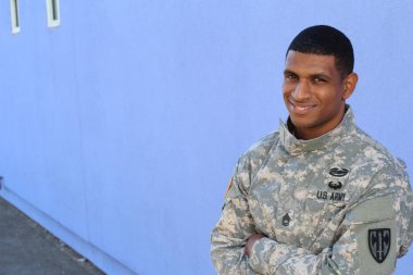 Mavi duvarın önünde üniformalı yakışıklı Afro-Amerikan askerinin yakın plan portresi