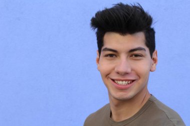 Mavi duvarın önünde poz veren yakışıklı genç adamın yakın plan portresi.