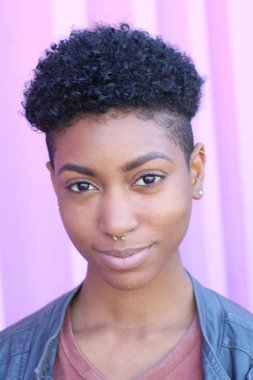 Mor duvar arkasında kısa kıvırcık saçlı güzel bir Afrikalı kadının yakın plan portresi. 