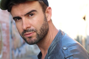 Genç, çekici bir hippi ve modaya uygun görünüşlü bir adam gülümsüyor. Mutlu pozlar veriyor. Gayri resmi giyiniyor, beysbol şapkası ve sakal takıyor.