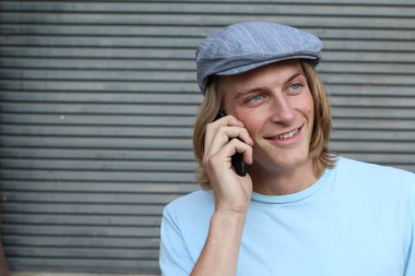 Sokakta telefonla konuşan, uzun saçlı, yakışıklı bir genç adamın yakın plan portresi.