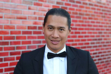 Kırmızı tuğla duvarın önünde papyonlu yakışıklı Asyalı bir adamın yakın plan portresi.