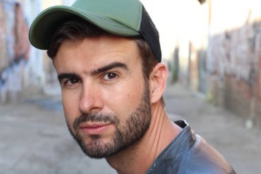 Genç, çekici bir hippi ve modaya uygun görünüşlü bir adam gülümsüyor. Mutlu pozlar veriyor. Gayri resmi giyiniyor, beysbol şapkası ve sakal takıyor.