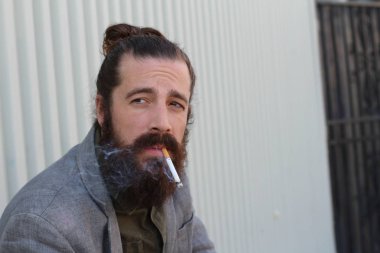 Sigara içen yakışıklı sakallı adamın portresi. Erkek saçı olan hippi..