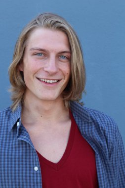 Mavi duvarın önünde uzun sarı saçlı yakışıklı genç adamın yakın plan portresi.