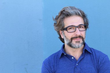 Mavi duvarın önündeki yakışıklı yetişkin adamın yakın plan portresi.