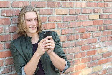 Uzun saçlı, yakışıklı genç bir adamın sokakta akıllı telefon kullanarak yakın plan portresi.