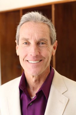 Bej ceketli yakışıklı olgun bir adamın kameraya bakarken yakın plan portresi.