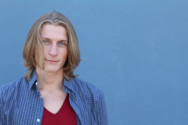 Mavi duvarın önünde uzun saçlı yakışıklı ve şık bir adamın yakın plan portresi.