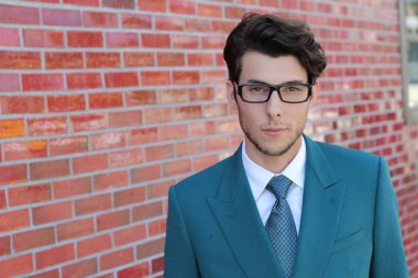 Mavi takım elbiseli ve kırmızı tuğlalı duvarın önünde gözlüklü yakışıklı iş adamının yakın plan portresi.