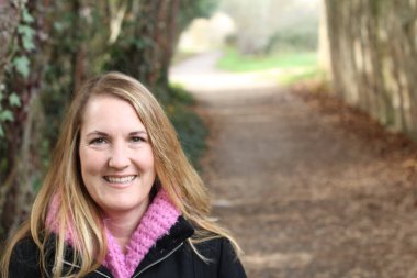 Güler yüzlü sarışın kadın güz parkında gündüz vakti duruyor.