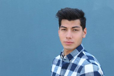 Mavi duvarın önünde poz veren yakışıklı genç adamın yakın plan portresi.