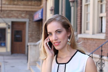 Güzel, güler yüzlü bir sarışın şehir dışında telefonla konuşuyor. 