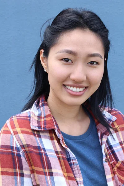 Closeup portrait of young beautiful Asian woman with long black hair and fresh natural makeup on blue background