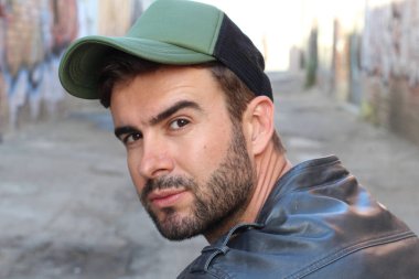 Genç, çekici bir hippi ve modaya uygun görünüşlü bir adam gülümsüyor. Mutlu pozlar veriyor. Gayri resmi giyiniyor, beysbol şapkası ve sakal takıyor.