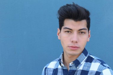 Mavi duvarın önünde poz veren yakışıklı genç adamın yakın plan portresi.