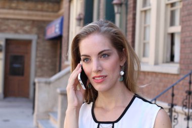 Güzel, güler yüzlü bir sarışın şehir dışında telefonla konuşuyor. 