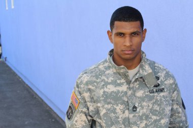 Mavi duvarın önünde üniformalı yakışıklı Afro-Amerikan askerinin yakın plan portresi