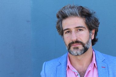 Mavi duvarın önünde pembe gömlekli yakışıklı yetişkin bir adamın yakın plan portresi.