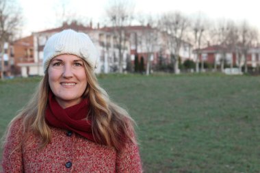 Kış giysileri içinde gülen sarışın kadının portresi gündüz vakti parkta duruyor.