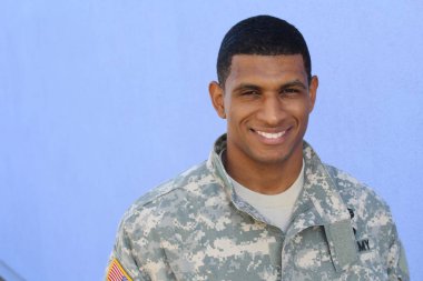 Mavi duvarın önünde üniformalı yakışıklı Afro-Amerikan askerinin yakın plan portresi