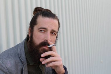 Sigara içen yakışıklı sakallı adamın portresi. Erkek saçı olan hippi..