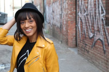 Lifestyle photo shoot portrait of cool trendy stylish sexy hipster African ethnic girl with septum piercing ring. Wearing yellow leather jacket and a hat