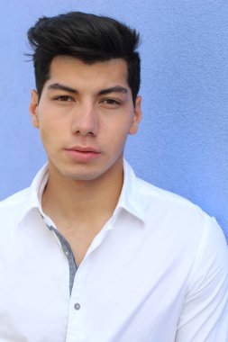 Mavi duvarın önünde poz veren yakışıklı genç adamın yakın plan portresi.