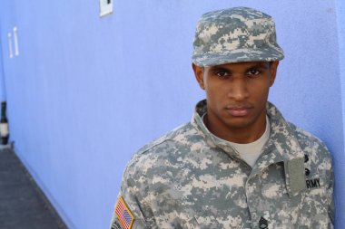 Mavi duvarın önünde üniformalı yakışıklı Afro-Amerikan askerinin yakın plan portresi