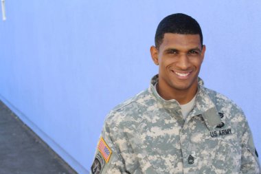 Mavi duvarın önünde üniformalı yakışıklı Afro-Amerikan askerinin yakın plan portresi