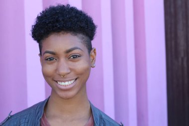 Mor duvar arkasında kısa kıvırcık saçlı güzel bir Afrikalı kadının yakın plan portresi. 