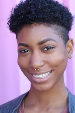 Mor duvar arkasında kısa kıvırcık saçlı güzel bir Afrikalı kadının yakın plan portresi. 