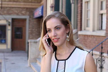 Güzel, güler yüzlü bir sarışın şehir dışında telefonla konuşuyor. 
