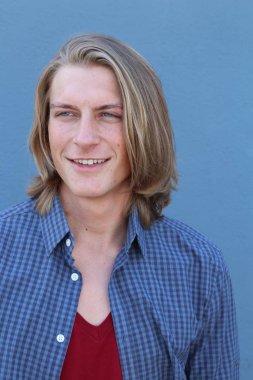 Mavi duvarın önünde uzun sarı saçlı yakışıklı genç adamın yakın plan portresi.