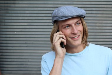 Sokakta telefonla konuşan, uzun saçlı, yakışıklı bir genç adamın yakın plan portresi.