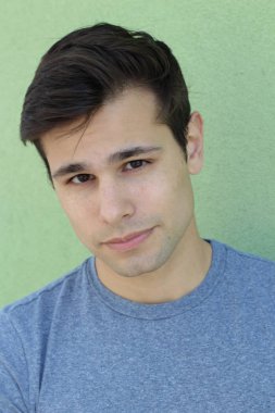 Yeşil duvarın önünde sıradan kıyafetler giymiş yakışıklı genç adamın yakın plan portresi.