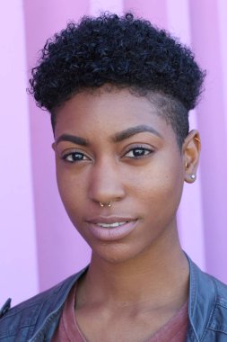 Mor duvar arkasında kısa kıvırcık saçlı güzel bir Afrikalı kadının yakın plan portresi. 