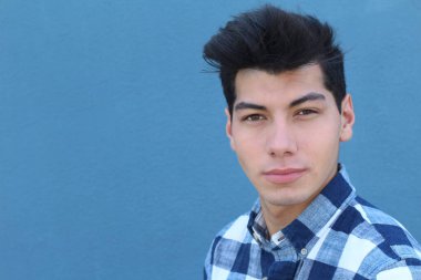 Mavi duvarın önünde poz veren yakışıklı genç adamın yakın plan portresi.